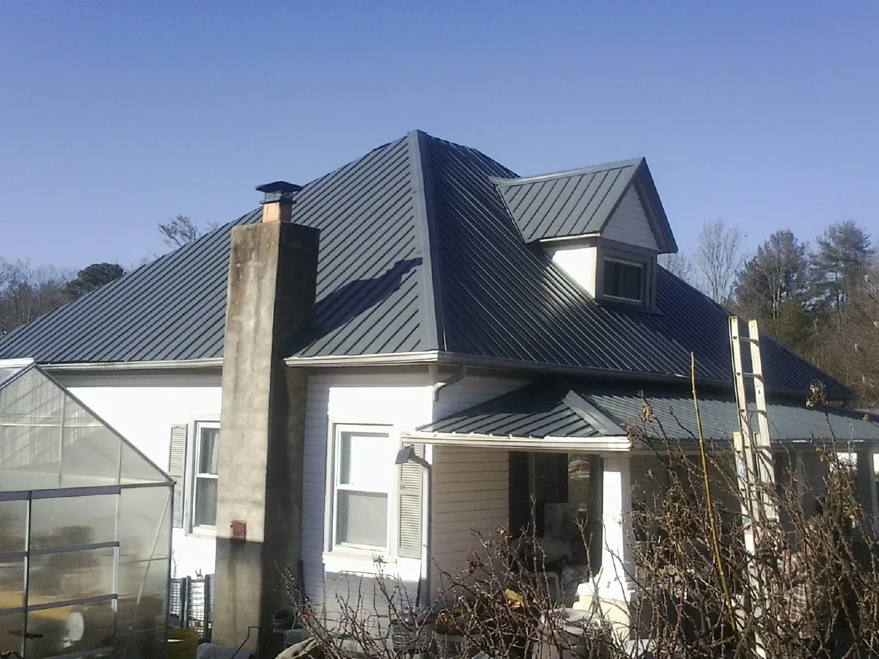 Dark blue standing seam metal roof on a white farmhouse with dormer — Slate & Tile Roof Repair by Roofing Brothers in Castle Hayne