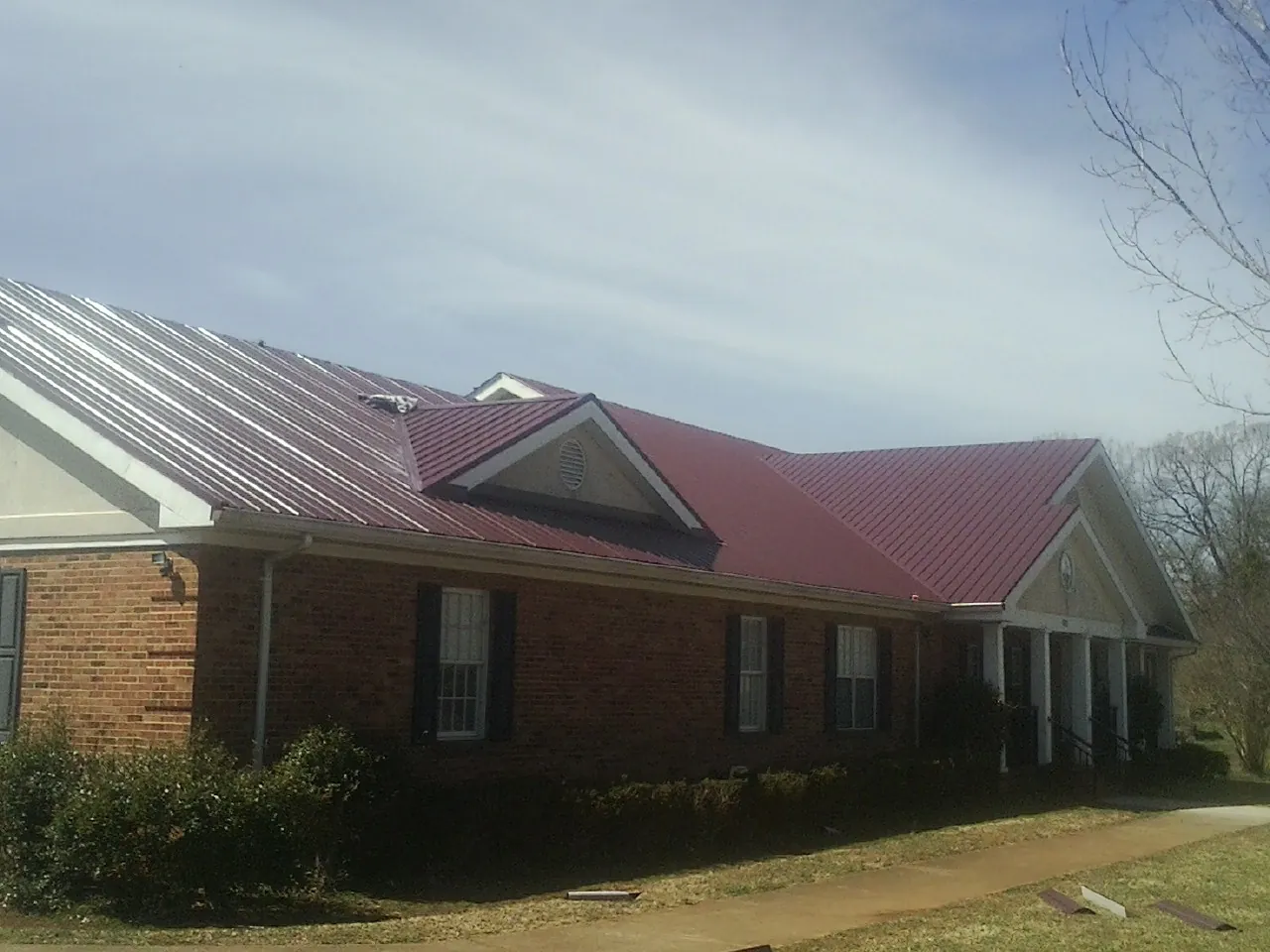 Red metal roof with gabled entries on a long brick building, from a Hail Damage Roof Repair job in Castle Hayne