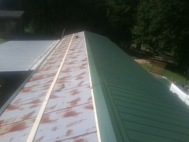 Old rusted panels beside newly installed green metal roofing in Castle Hayne