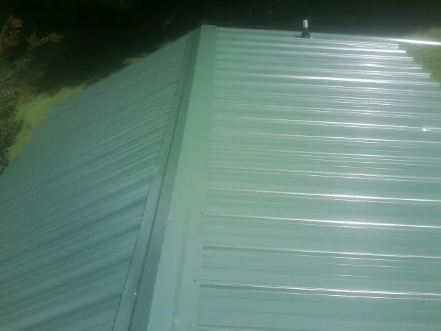 New green metal panels meeting at the ridge of a roof — Flat Roof Repair work by our crew in Castle Hayne