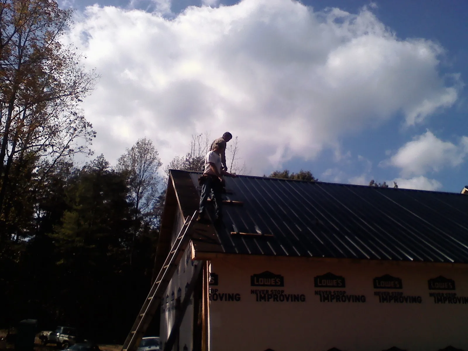 Roofer fastening dark metal panels high against a cloudy sky, from a Roof Inspection job in Castle Hayne