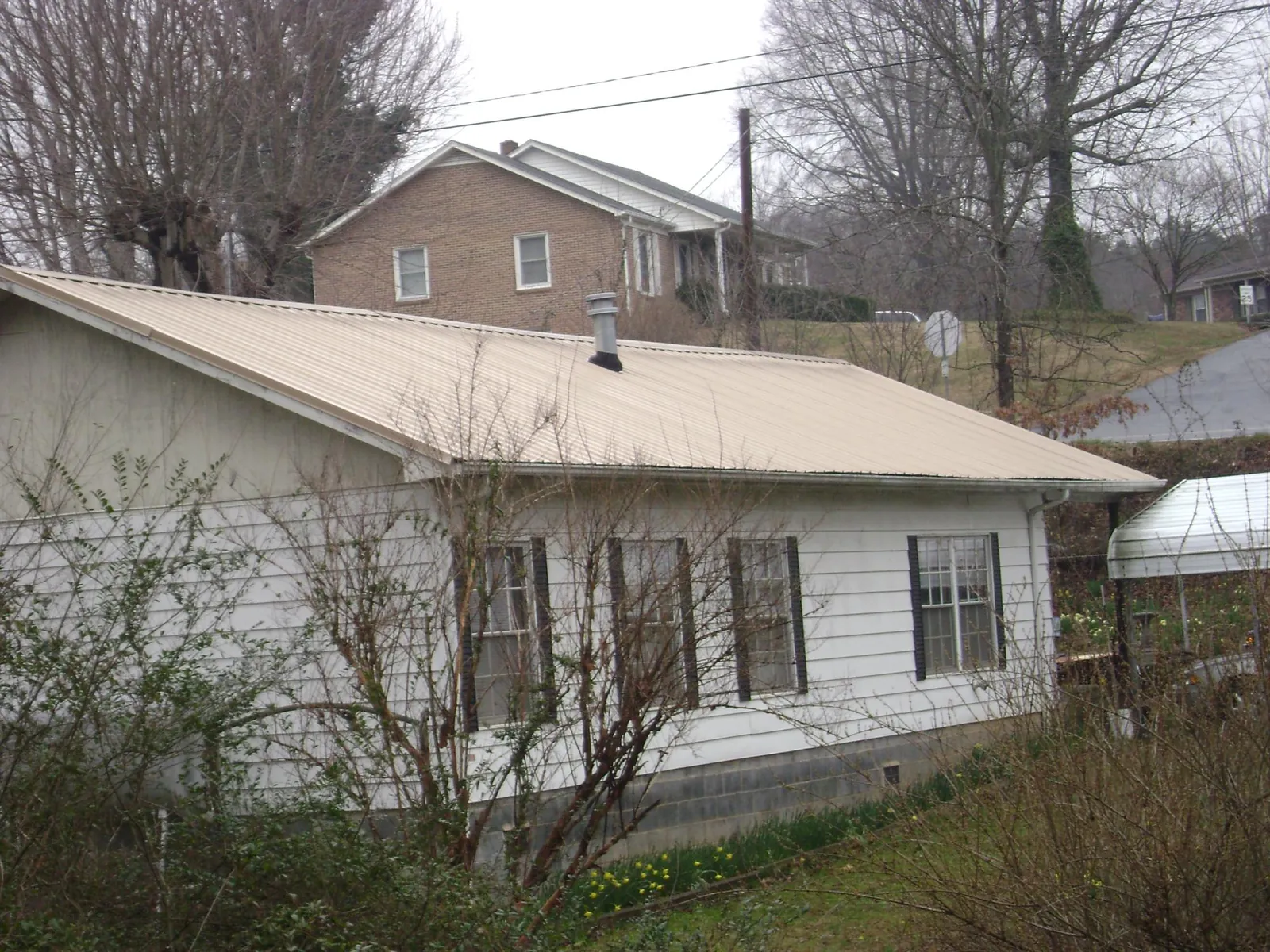 Tan metal roof on a white sided house set into a hillside — Commercial Roofing by Roofing Brothers in Castle Hayne