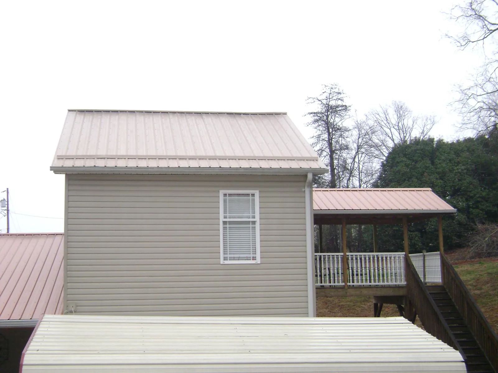 Tan metal roofs on a two story addition and attached porch, from a Roof Replacement job in Castle Hayne